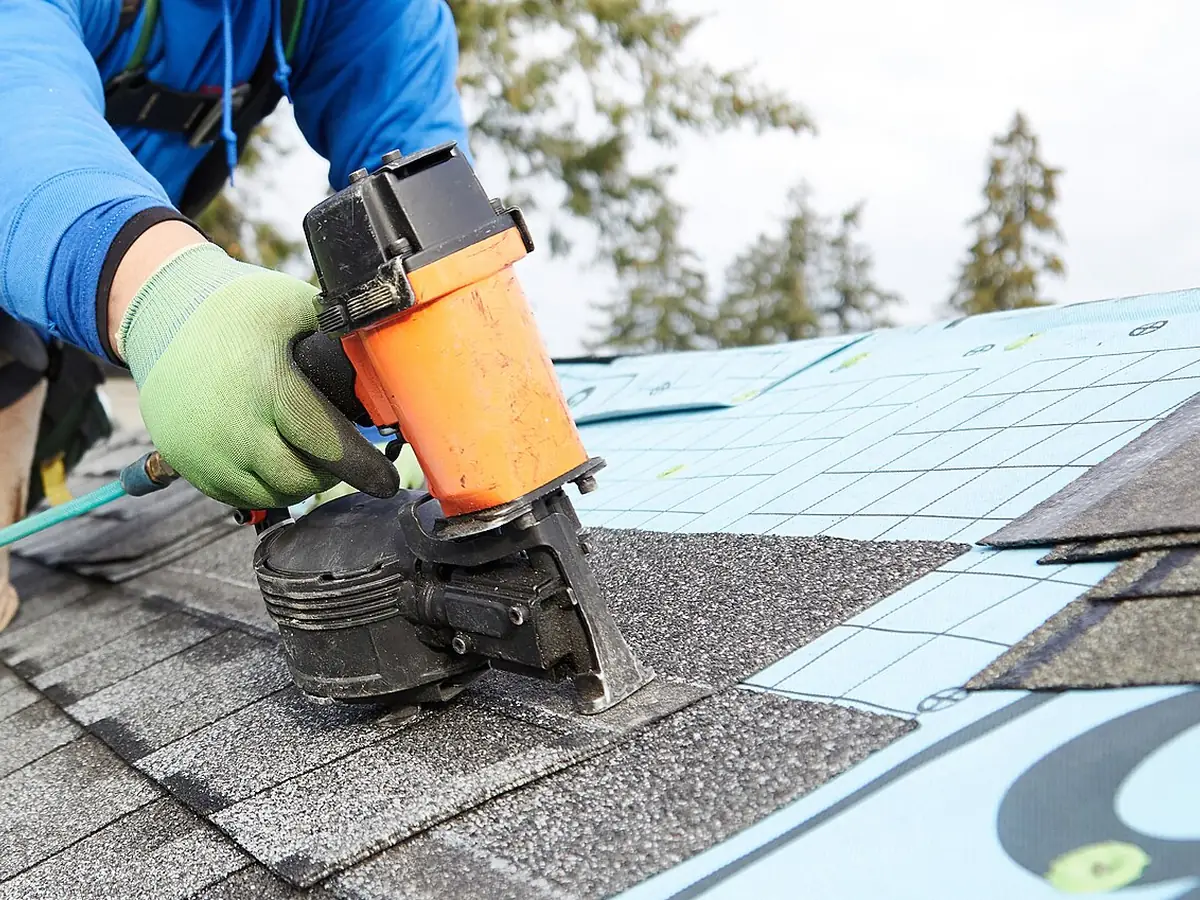 Roofer using a nail gun on new asphalt shingles