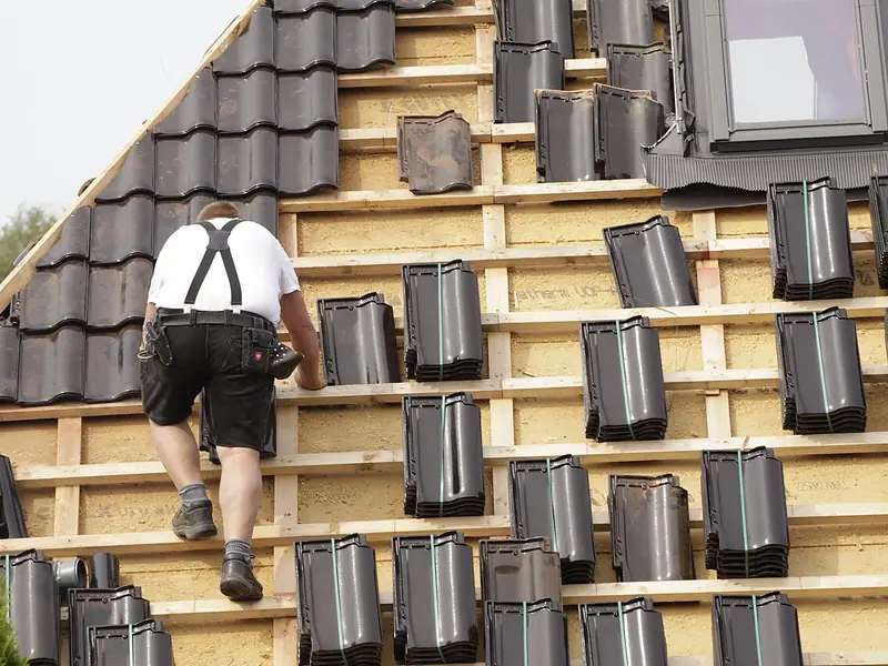 Roofer carrying tiles across new roof battens
